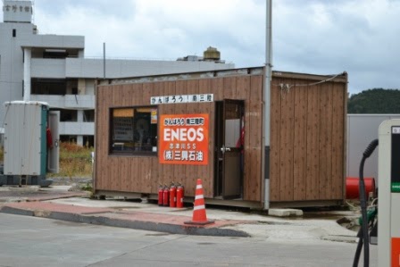 ENEOSのオレンジ色の看板が掲げられた木目調のプレハブの仮設店舗で、赤い消火器が4つ店舗前に置かれている仮設店舗を写した写真