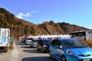 山あいの道路にたくさんの乗用車や軽トラックが連なり、鮭まつり福興市の会場に向かって並んでいる写真