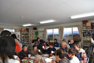 地域住民や関係者が一つの部屋に集まり、テーブルを囲んでお茶を飲みながら語り合っている懇談会の様子の写真