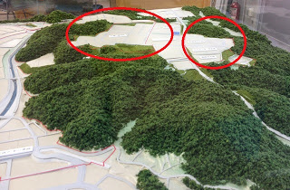 森林に囲まれた山間部の模型の写真中、奥にある平坦地が2か所赤い丸で囲まれ示されている画像