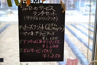 白とピンクのチョークで「本日のサービスランチセット」とメニューが手書きされた黒板が窓に吊り下げられている写真