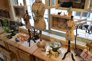 アクセサリーや雑貨が飾られている3体の小さいトルソーが木製の棚に置かれた、手作り雑貨の陳列スペースの写真