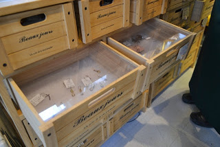 棚に並んだ木箱の引き出しを引き出すと、アクリル製の透明な蓋越しに、小さなアクセサリー類が整然と並んでいる様子が見えるディスプレイの写真