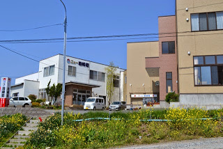 道路を車が数台走行している両側に、茶色い建物と壁に「ニュー泊崎荘」と書かれた白い建物が並んでいる写真