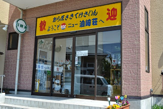 レンガ調の入口上に「歓迎 ようこそニュー泊崎荘へ」と黄色い看板が掲げられている旅館の正面入口の写真