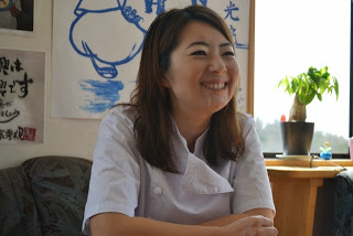 白衣を着た高橋宮倫子さんが笑顔で椅子に座ってインタビューを受けている様子をアップで撮影した写真