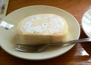 皿の上にフォークと一緒に置かれた、刻んだワカメが入ったクリーム入りのロールケーキがテーブルに乗っている写真