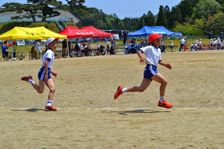 白い体操着と赤白帽をかぶった児童が校庭を力強く走り、競走している写真