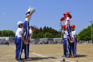 マイクスタンドが設置された白線を挟んで、赤と白のチームに分かれた馬の形を作った3人の児童が騎手を担ぎ、騎馬戦が開始されようとしている写真