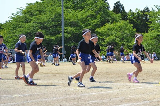 黒いシャツと青いズボンの児童たちが右足を前に出して、グラウンドで元気よくよさこいを披露している写真