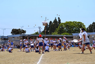 白い衣装を着た男子生徒が応援するなか、白い帽子を被った児童たちが、白い玉をカゴめがけて投げ入れている玉入れの様子の写真