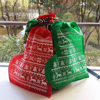 窓際の白い台の上に、白いトナカイや雪の結晶、木の模様がデザインされたクリスマス柄の赤と緑色の巾着袋が2つ並べられている写真