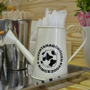 「SIZENTAMAGONOUEN SINCE 2004」と牛のロゴが入った白いジョウロ型の小物入れの写真