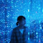 青い光の粒が無数に輝く幻想的な空間の中に目黒杏奈さんが立っている写真