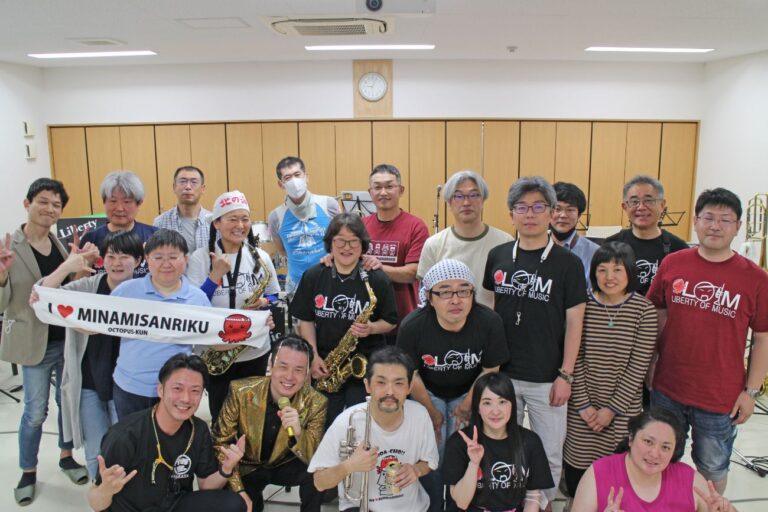 「I LOVE MINAMISANRIKU」と書かれた布や楽器を持った人たちの集合写真