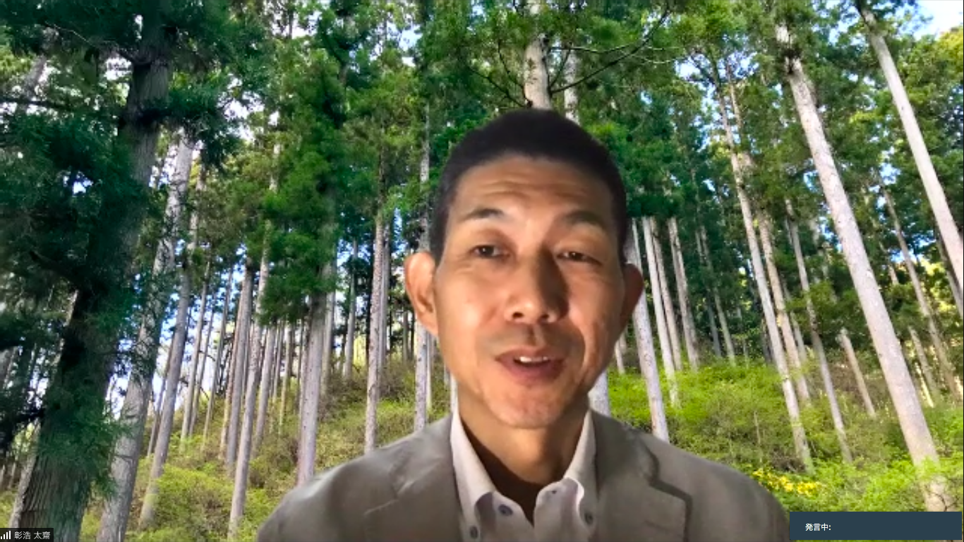森林のバーチャル背景を使ったオンライン会議で、グレーのジャケットを着た太齋 彰浩さんが穏やかな表情で話をしている画面