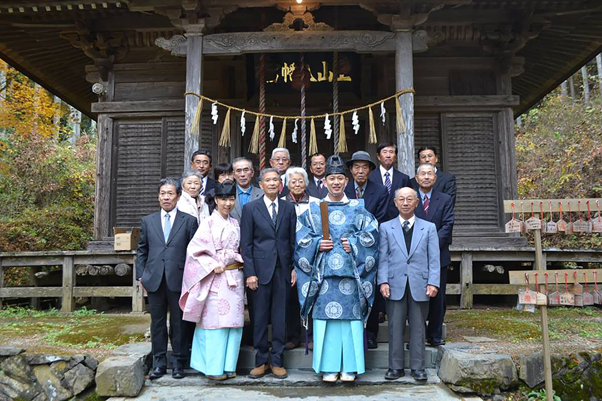 神社の前で、装束を着た工藤さんご夫婦と正装した男女が並んで写っている集合写真