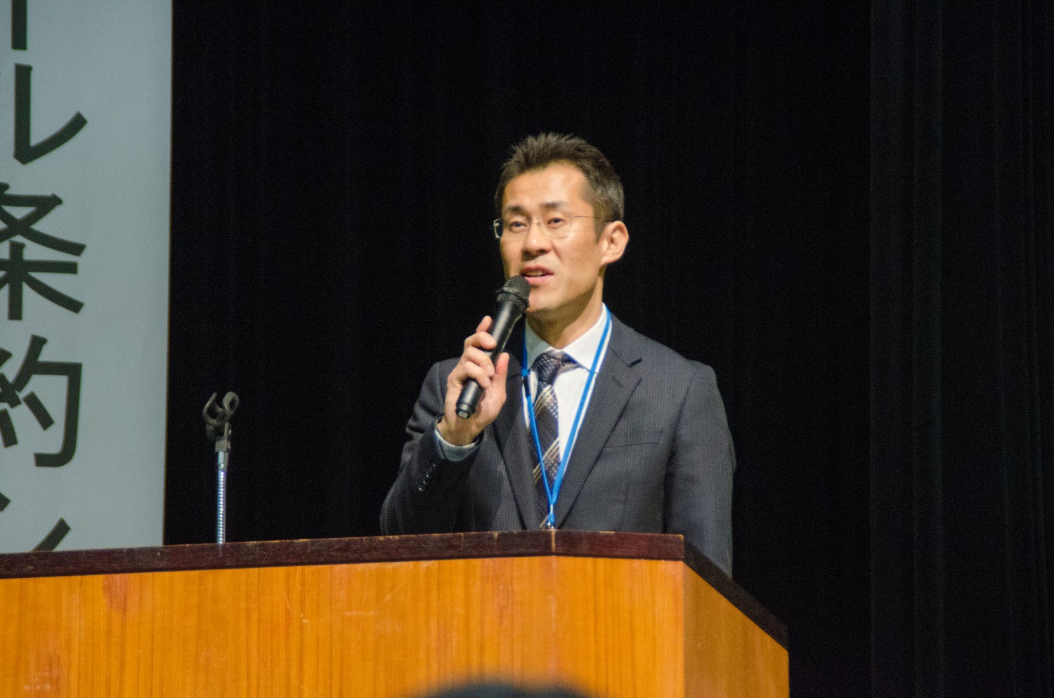 演題に立ち、マイクを持って話をしている阿部拓三さんの写真