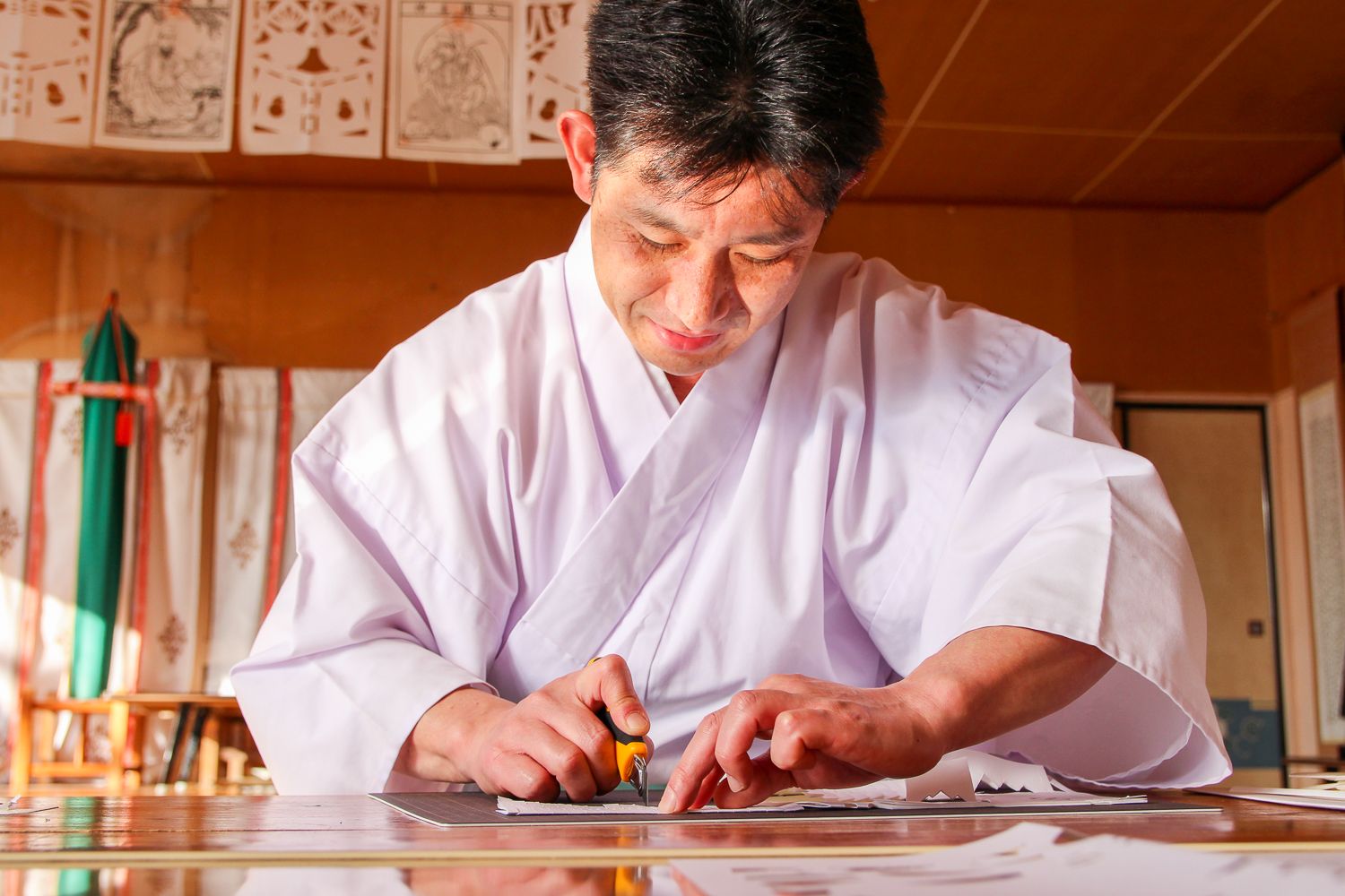 白い和紙が机の上に広げられ、工藤庄悦さんが真剣な表情でカッターを使い、ゆっくりと丁寧に線を切って作成する様子の写真