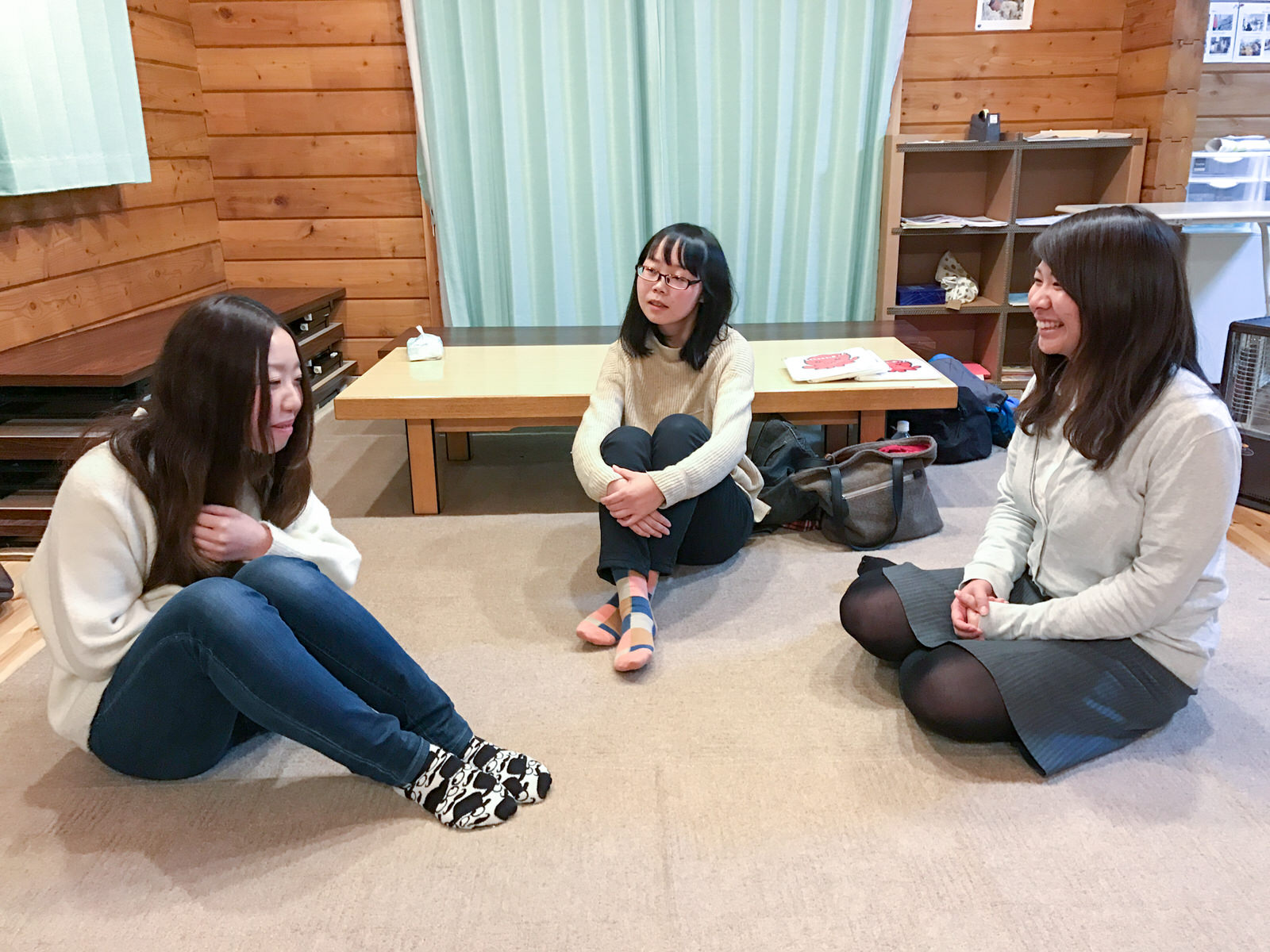 三人の女性が室内で床に座って談笑している写真