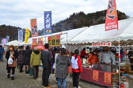 たくさんの屋台が並び、大判焼きや牛タン串などの旗が立ち並ぶ中、来場者が屋台料理を楽しんでいる写真