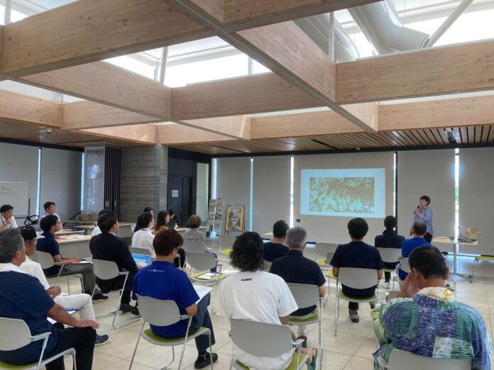 室内で複数の人が座ってスライドを見ながら講義を聞いている様子の写真