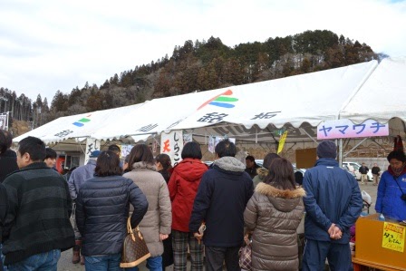 来場者が列を作り、さまざまなテントで地元の特産品や食べ物を買い求めている写真