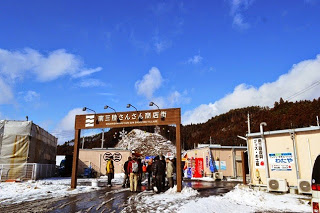 木製の門に「南三陸さんさん商店街」と書かれ、雪がまだ積もった入り口付近に人が集まっている写真