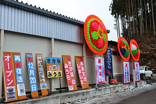 建物の外壁に新装開店を知らせる看板や垂れ幕が並び、大きな花輪が飾られている様子の写真