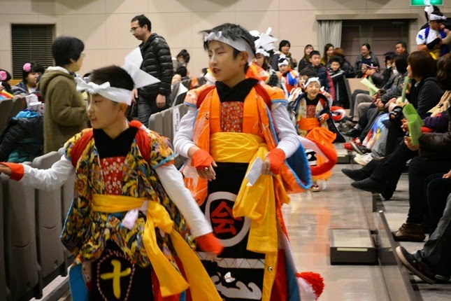 色鮮やかな伝統衣装を身にまとった子どもたちが、室内の観客の間を練り歩いている様子の写真