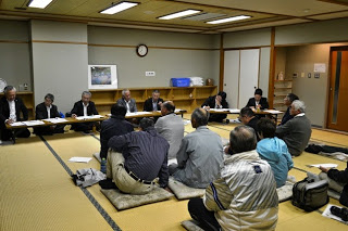 和室の畳に座布団が並べられ、中央に地域の方々が座って話を聞いており、正面には資料を前にしたスーツ姿の関係者らが並んで座っている、南三陸町議会と住民との懇談会の写真