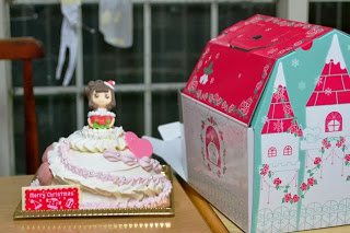 ドレス姿の人形が乗った華やかなドールケーキとお城風デザインの可愛らしいケーキの箱が机の上に置かれている写真