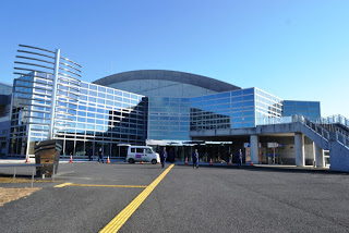 雲ひとつない青空の下、建物右側には屋外階段がある、大きなガラス張りの外壁とアーチ型の屋根を持つ近代的な建物ベイサイドアリーナの写真