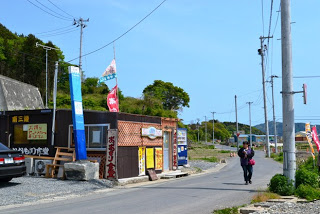 人が歩いている道路の傍に商店と青い柱のような案内表示が立っている写真