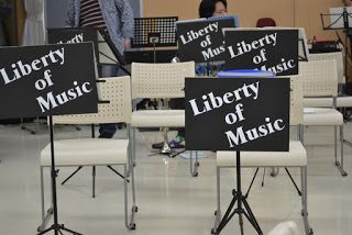 「Liberty of Music」と大きく書かれた黒い譜面台がいくつも並んでいて、演奏の準備が整えられている音楽会場内の写真