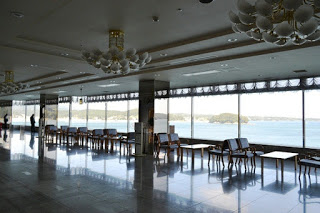 広いロビーの大きな窓から海と島々が一望でき、テーブルと椅子が整然と並べられている静かな休憩スペースの写真