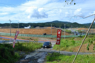 草が茂る小道の先に黒い車が停まり、「八幡宮」と書かれたのぼり旗が立っている八幡宮付近の風景の写真