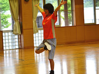 体育館の床の上で、片足を上げて両腕をあげてバランスを取っている阿部純子さんの写真