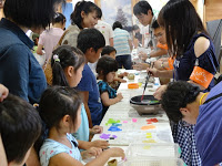 子供たちがテーブルに並んで座り、紙や道具を使って楽しそうに工作をしている様子を写した写真