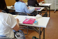 数人の参加者が裁縫道具や布などが置かれた机に向かって座っている講習会の様子の写真