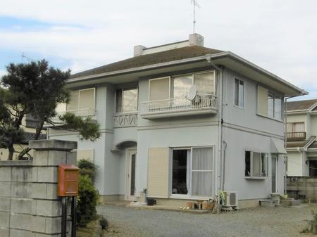 二階に小さなバルコニーがある薄いグレーの外壁と切妻屋根を持つ二階建て住宅の写真