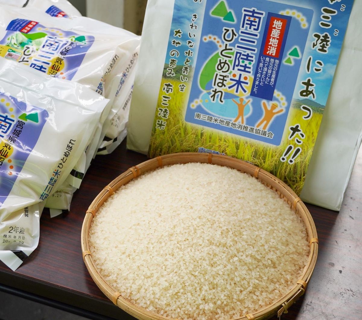 丸い竹のざるに精米された白くつややかな米粒が盛られており、後ろには「南三陸米ひとめぼれ」と書かれたパッケージの米袋が置かれた写真