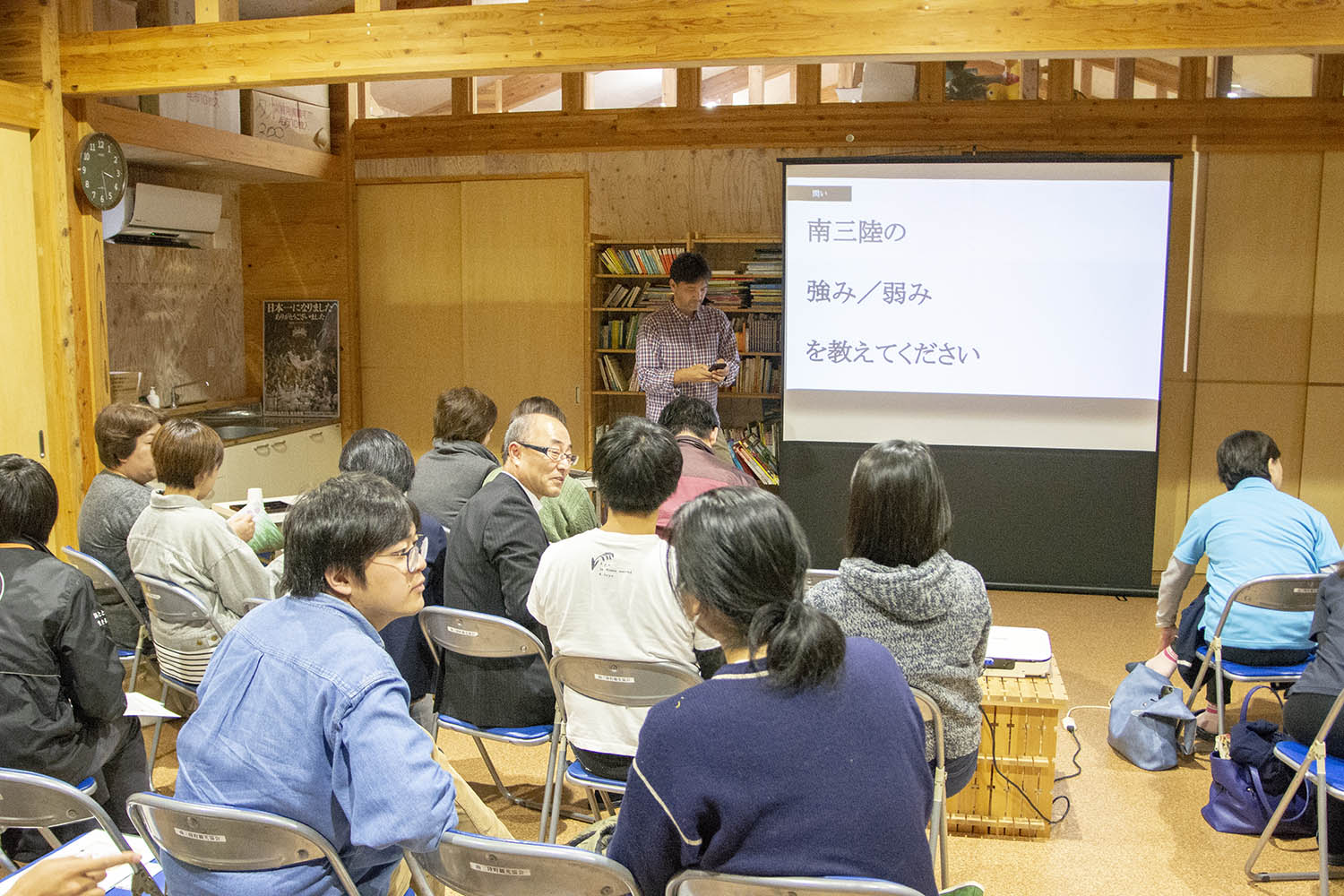 木造の室内で複数の人が椅子に座ってスクリーンに映し出された「南三陸の強み/弱みを教えてください」という日本語の質問文を見ながら講義を受けている様子の写真
