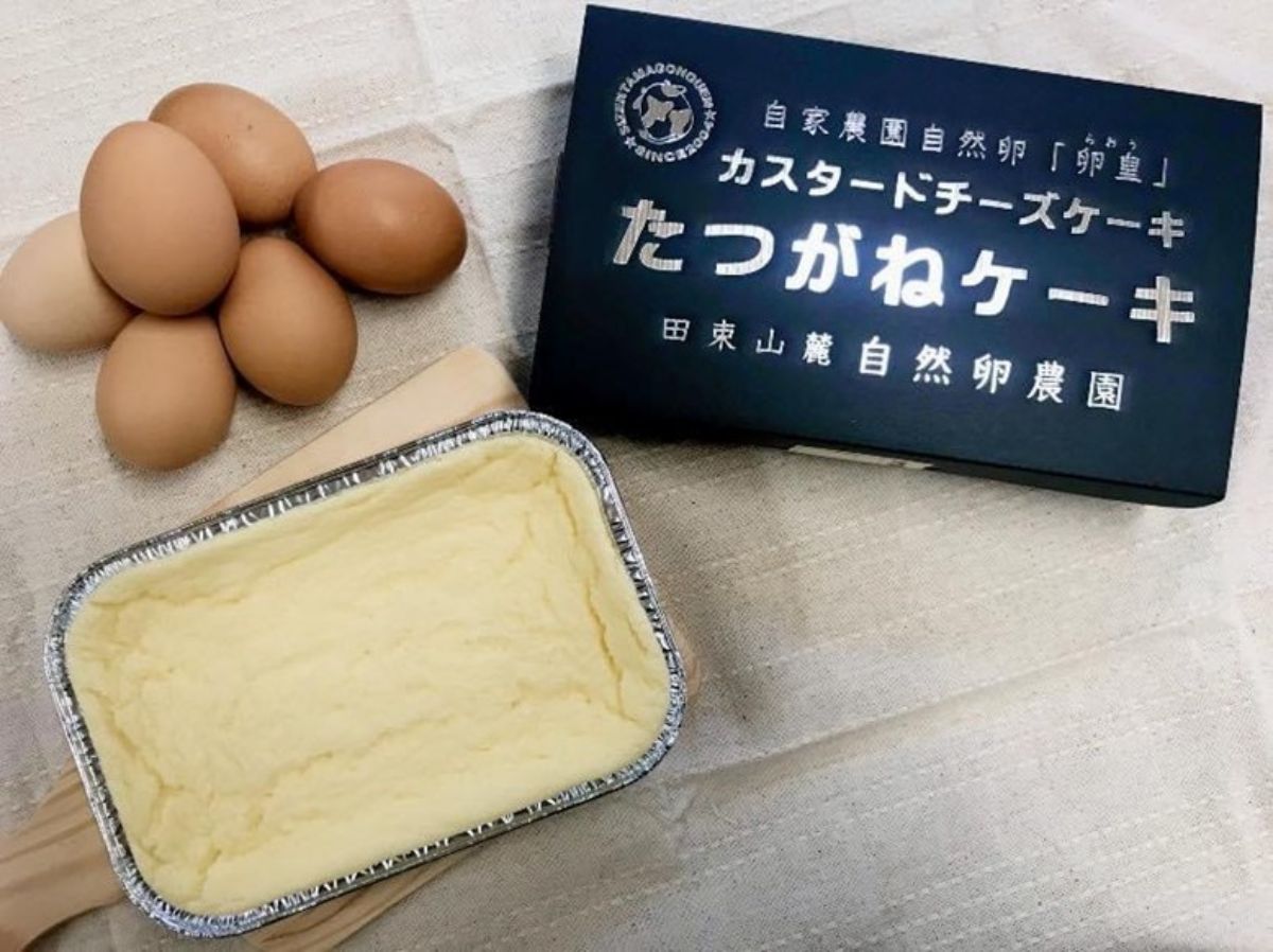 6個の茶色の卵が重ねられ、その隣に黒い箱に銀色の文字でカスタードチーズケーキ たつがねケーキと書かれた箱、銀のトレイに入ったカスタードチーズケーキが置かれている写真
