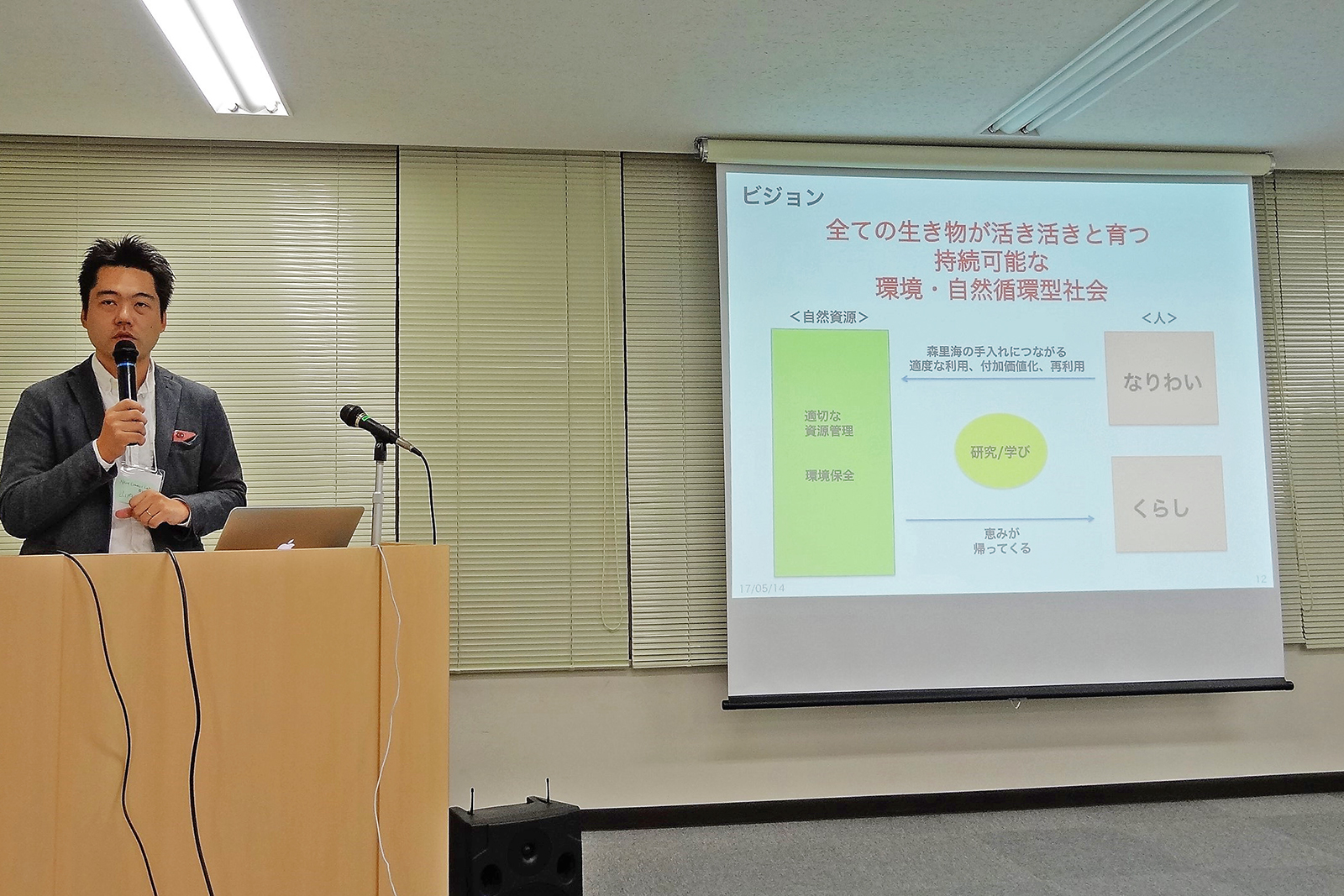 資料が映し出されたスクリーンの横に設置された演台に立ち、マイクを持って話をしている山内さんの写真