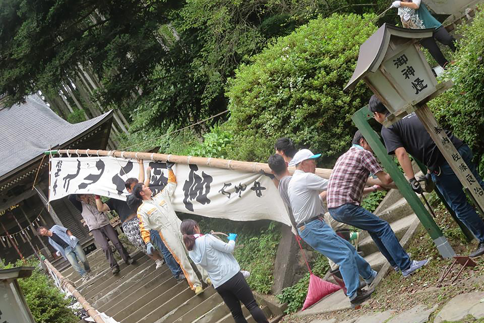 階段の上から下に向かって多くの人々が協力して大きな竹の棒の旗を運んでいる写真