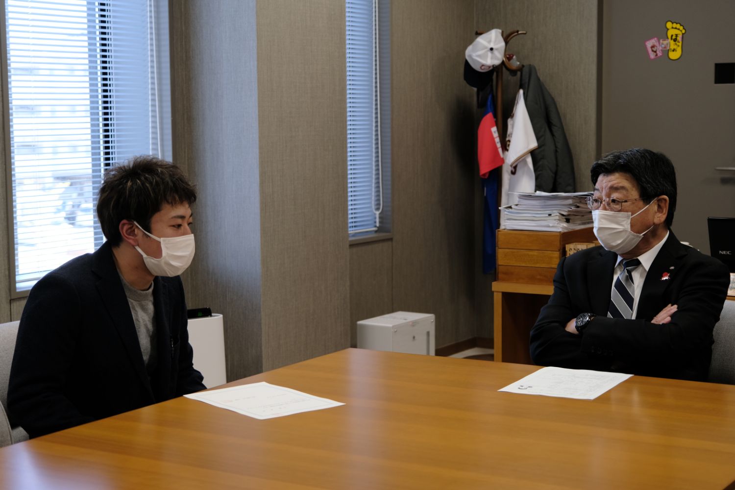 紺色のジャケットの佐藤さんとスーツ姿の南三陸町長が、室内の会議室に座り、それぞれの前に書類が置かれ話をしている写真