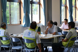 黄緑色のビブスを着た関係者たちが議室でテーブルを囲み、打ち合わせをしている様子の写真