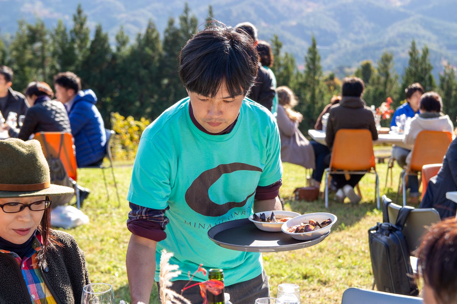 ブルーのTシャツを着た正司勇太さんが、黒いトレイに料理の乗った皿を持って配っている写真