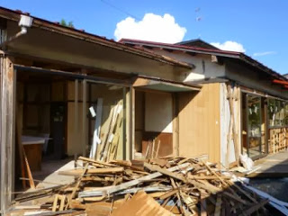 建物の一部が壊れ、木材の破片が散乱している改装前の古民家外観の写真